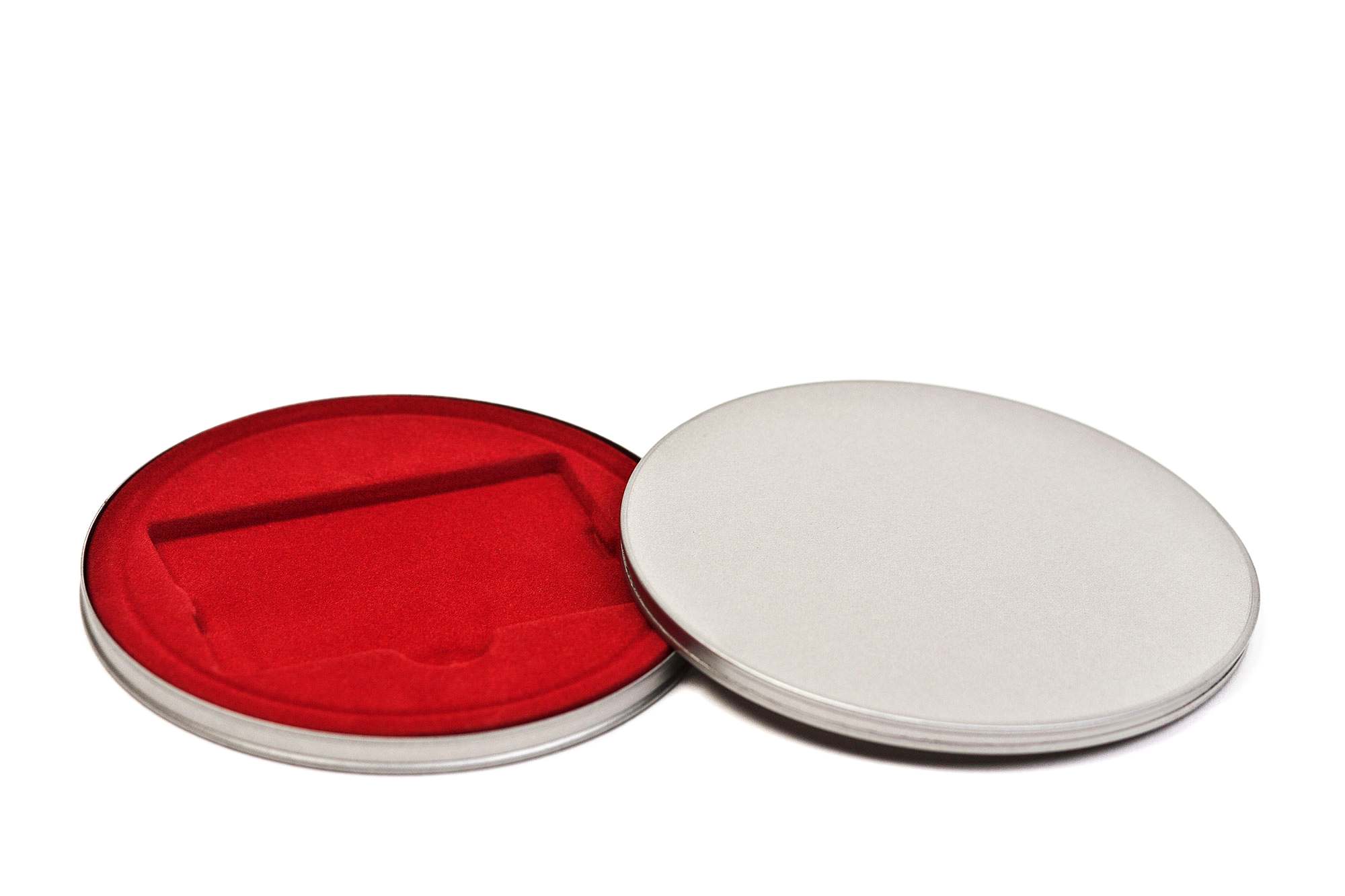 Boîte métallique ronde ouverte en métal couleur argent avec insert en velours rouge, photographiée sur fond blanc.