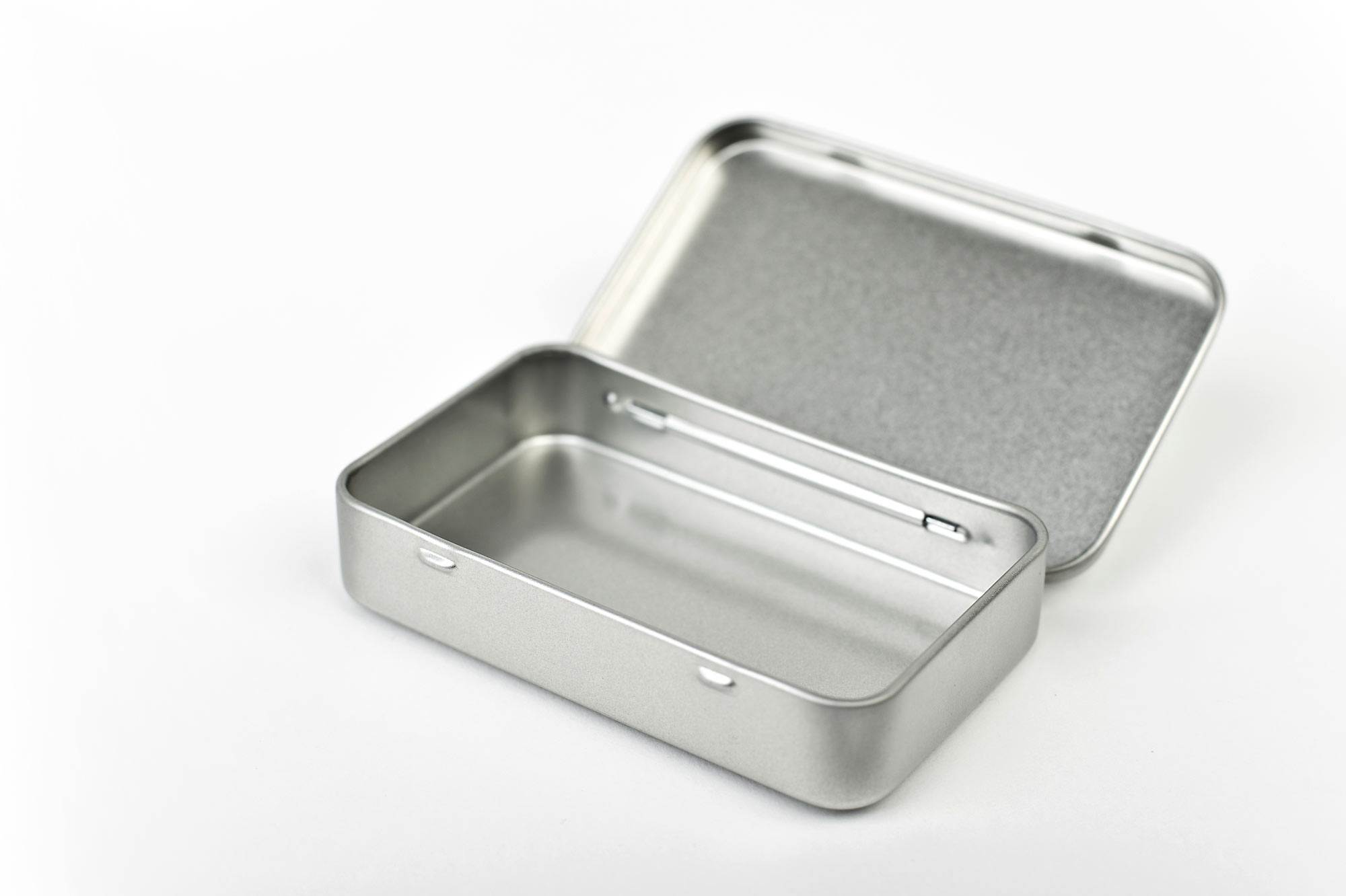 Boîte de poche plate ouverte en métal couleur argent avec couvercle à charnière, rectangulaire, photographiée sur fond blanc.