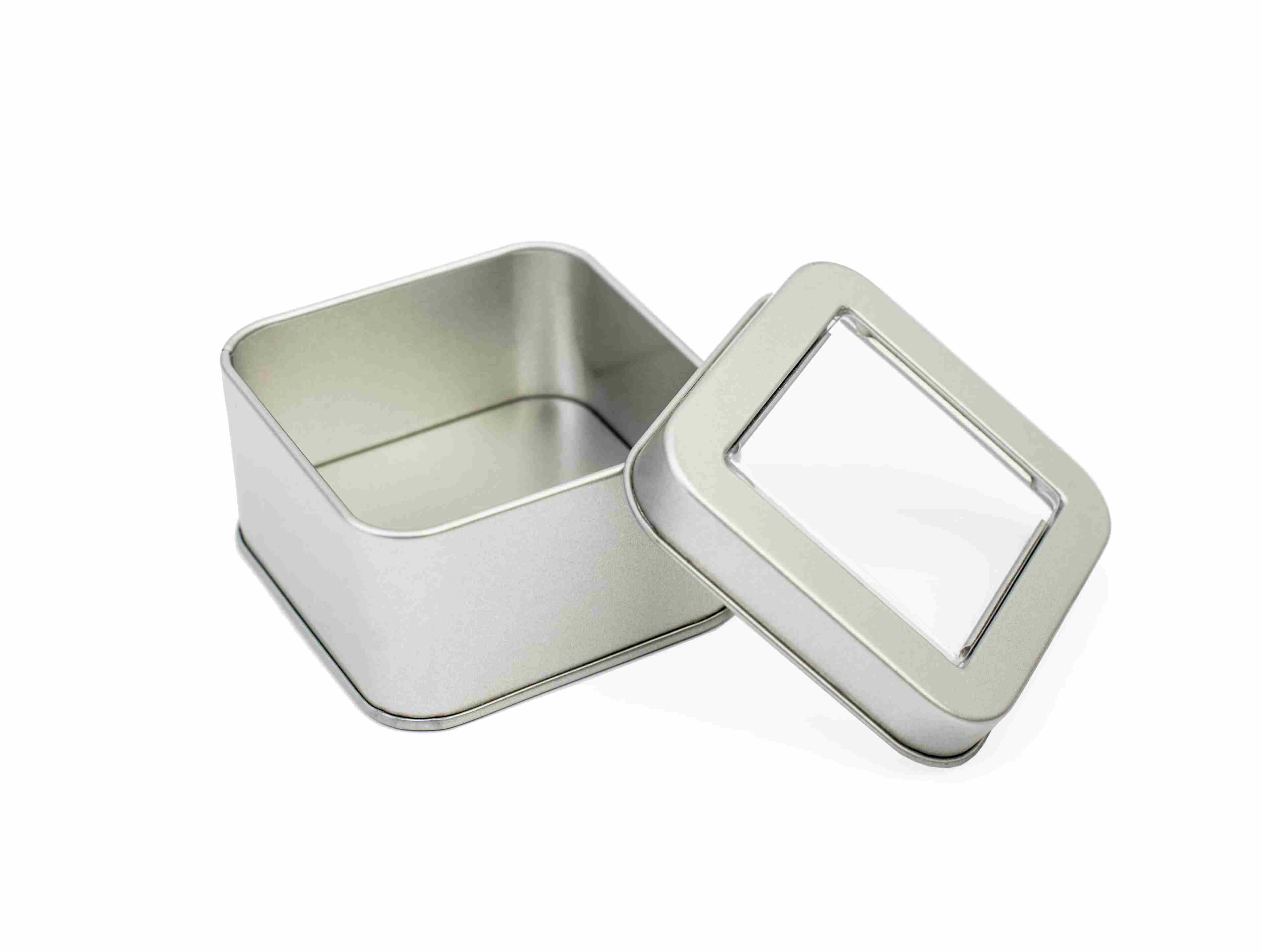 Boîte métallique carrée ouverte en argent avec couvercle retiré, doté d'une fenêtre transparente, photographiée sur fond blanc.