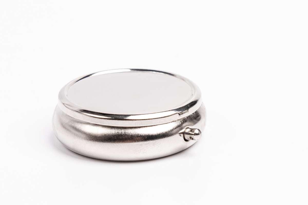 Cendrier de voyage rond fermé en métal couleur argent avec fermeture à bouton-pression, photographié sur fond blanc.