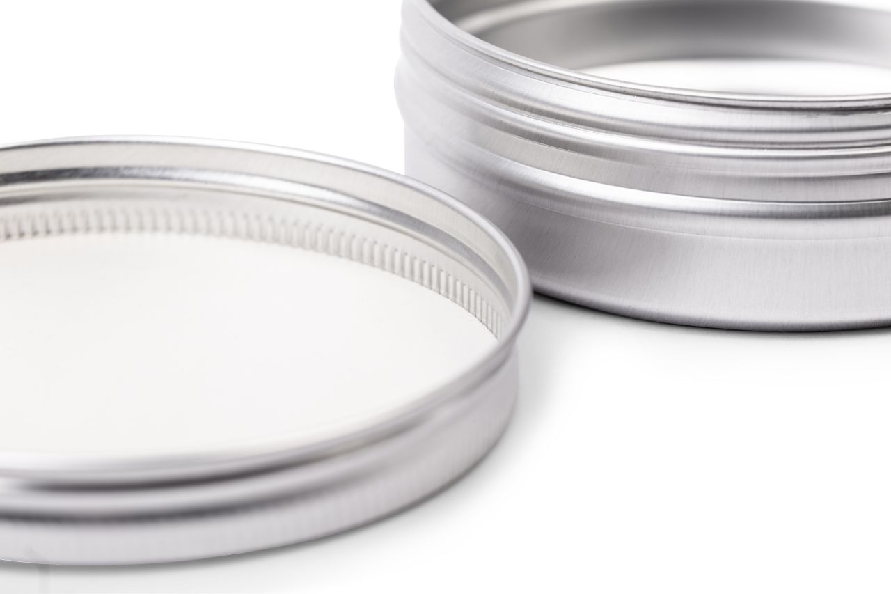 Gros plan d'une boîte en aluminium argenté ouverte avec volume de 125 ml. Le focus porte sur le filetage à vis et l'intérieur du couvercle, qui montre une crème blanche.
