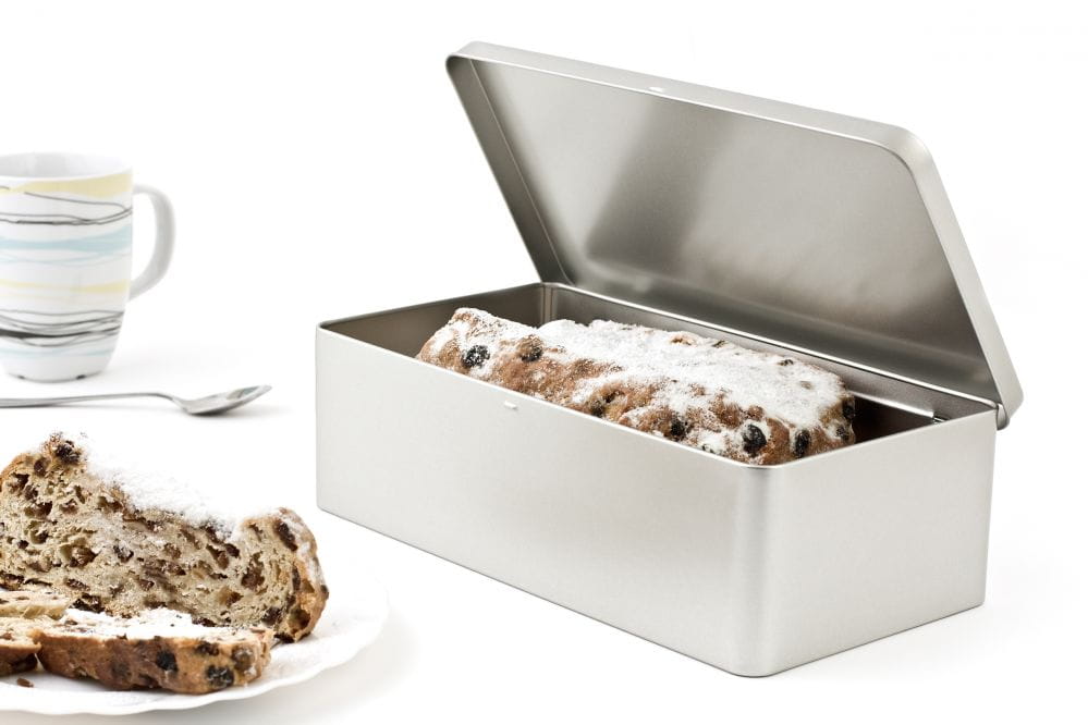 Boîte métallique rectangulaire ouverte avec couvercle emboîtant retiré, remplie de stollen et de sucre en poudre, photographiée sur fond blanc.
