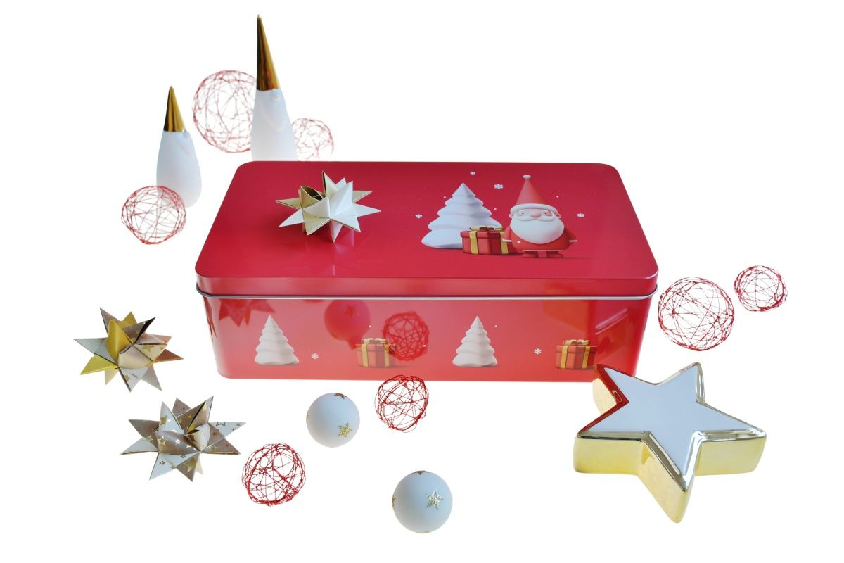 Boîte métallique rouge de Noël avec motifs festifs (Père Noël et sapins) sur le couvercle, entourée de décors de Noël comme des étoiles dorées et blanches, des boules de fil rouge et des ornements, fond neutre.