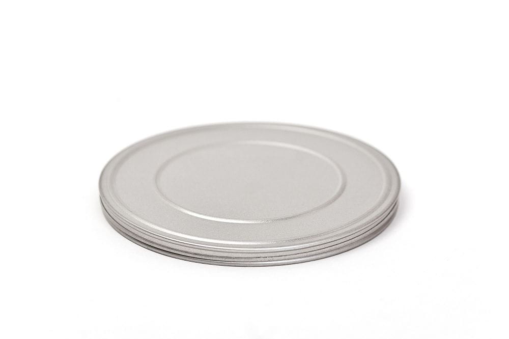 Boîte en fer blanc ronde fermée en métal argenté avec couvercle plat, photographiée sur fond blanc.