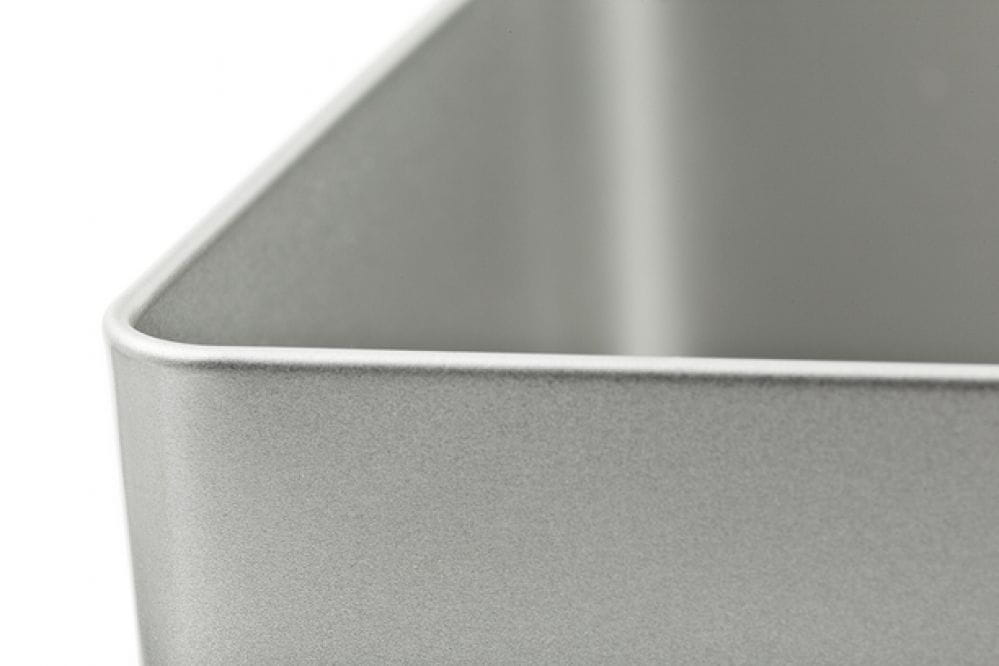 Boîte métallique carrée ouverte en tôle couleur argent avec couvercle emboîtant retiré, détail d'un coin, photographiée sur fond blanc.