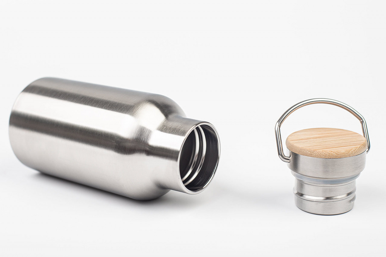 Bouteille à boire en acier inoxydable ouverte avec couvercle à vis amovible, couvercle avec insert en bambou et poignée en métal à charnière, photographiée sur fond blanc.