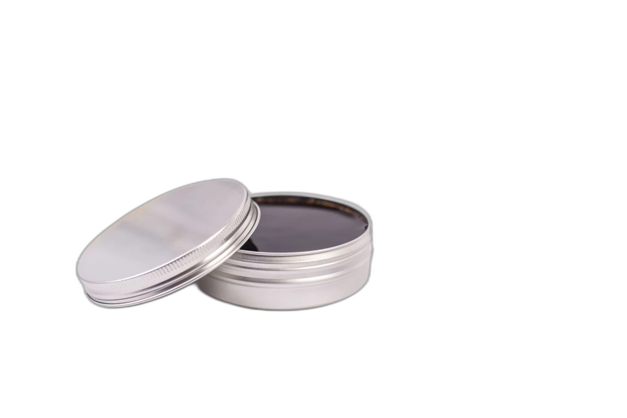Boîte en aluminium argenté ouverte avec capacité de 125 ml, remplie d'une substance foncée, possiblement huileuse. Le couvercle est légèrement appuyé et le fond est blanc.