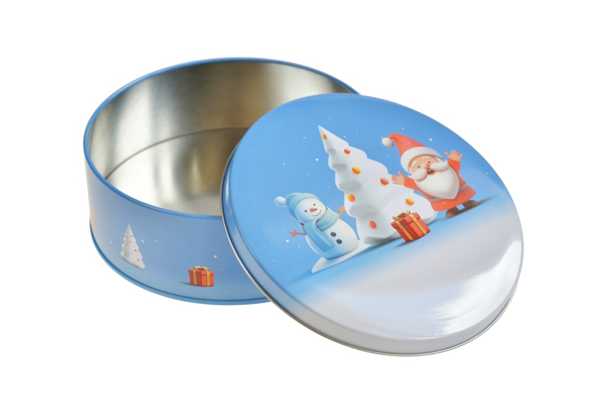 Boîte métallique ronde ouverte avec couvercle motif hivernal montrant un Père Noël, un bonhomme de neige et un sapin de Noël, posée sur fond blanc.