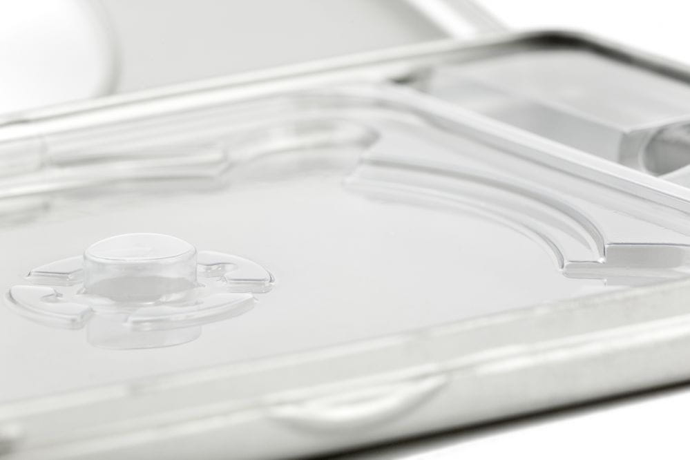 Détail d'une boîte métallique DVD ouverte avec plateau en plastique transparent et support de disque central, couleur argent, photographiée sur fond blanc.